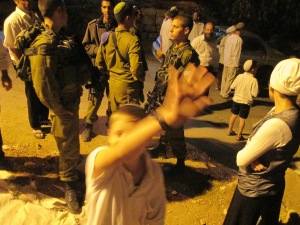An Israeli settler child hits my camera during the incident when settlers blockaded Palestinians in their home, and went on to attack us. Soldiers stand stand by in the background